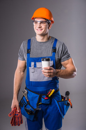 Construction work. Portrait of a young builder with tools in hand to build on gray backgroundの写真素材