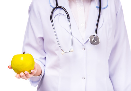 Portrait of a young beautiful woman doctor in white coat holding an apple isolated on a white backgroundの写真素材