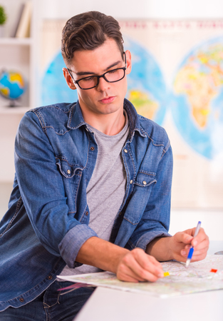 Portrait of a young man selects for the trip using a map sitting in office travel agencyの写真素材