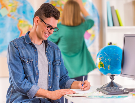 Portrait of a young man and woman chooses a place to travel through area, sitting in office travel agencyの写真素材