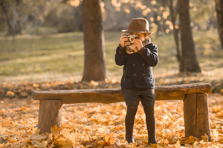 Little boy uses an old camera while walking in autumn parkの写真素材