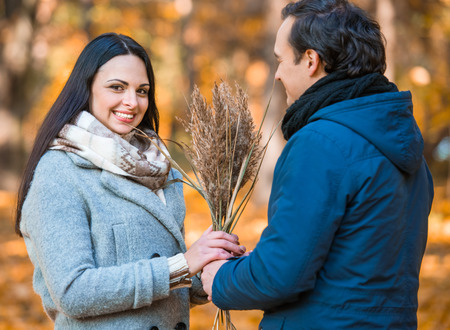 Young happy couple smiling during a walk in the park in autumn. From gives her dried flowersの写真素材