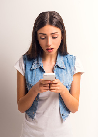 Portrait of cheerful girl teenager using the phone on a white backgroundの写真素材