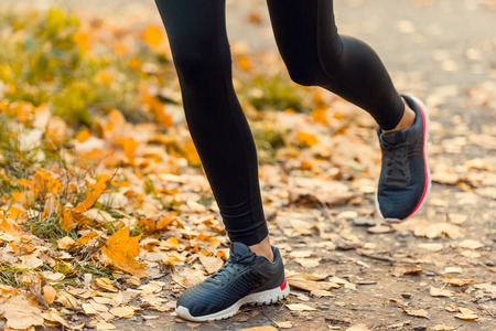 Young beautiful woman running in autumn park and listening to music with headphones. Legs close-upの写真素材