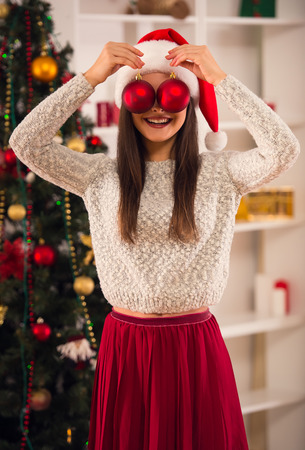 Young beautiful woman decorates Christmas tree celebrating Christmas at homeの写真素材