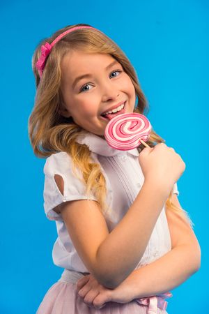 Portrait of a little girl with a big candy isolated on a blue backgroundの写真素材