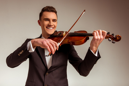 The young musician man playing violin on gray backgroundの写真素材
