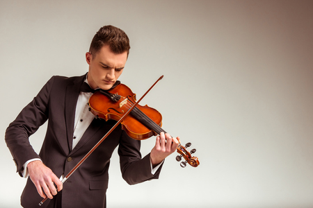 The young musician man playing violin on gray backgroundの写真素材