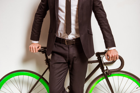Portrait of a young successful businessman in a business suit with a bicycle on a gray backgroundの写真素材
