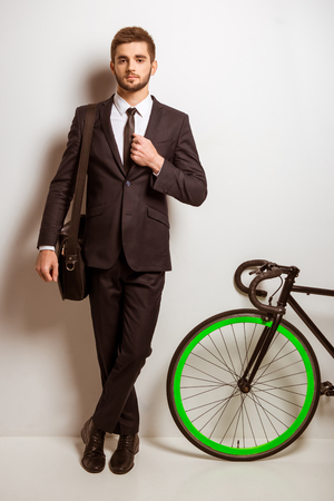 Portrait of a young successful businessman in a business suit with a bicycle on a gray backgroundの写真素材