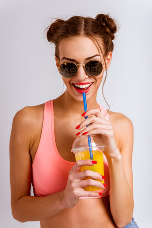 Portrait of a beautiful young girl drinking juice, isolated on gray backgroundの写真素材