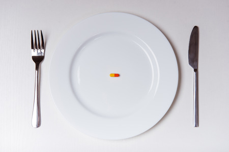 White plate with fork and knife lying on a white backgroundの写真素材