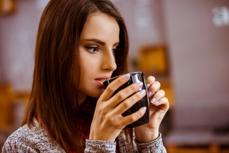 Beautiful young woman in casual clothes drinking coffee and dreaming while sitting in a cafe, close-upの写真素材