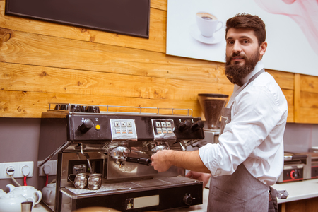 Young handsome barista with beard in shirt and bow tie making coffeeの写真素材