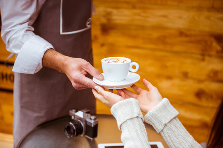 Young handsome waiter with beard giving a cup to young beautiful woman in a cafe, close-upの写真素材