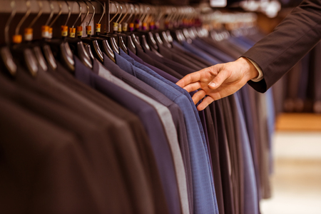 A hand of a modern young handsome businessman choosing classical suit from the row of suits in the suit shop, close-upの写真素材