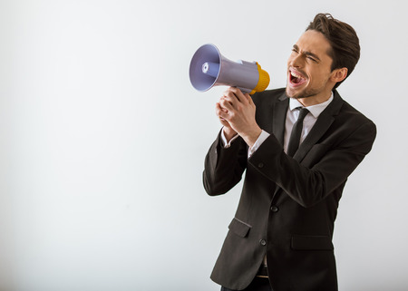 Handsome young businessman in classic suit screaming into loudspeaker, on white backgroundの写真素材