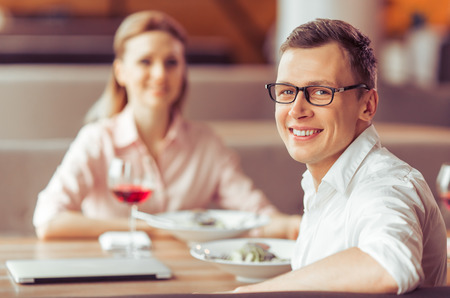 Handsome young businessman in eyeglasses is looking at camera and smiling during business lunch at the restaurantの写真素材