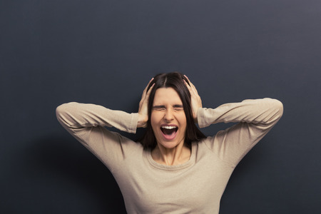 Beautiful young girl is covering ears with hands and screaming, standing against blackboard