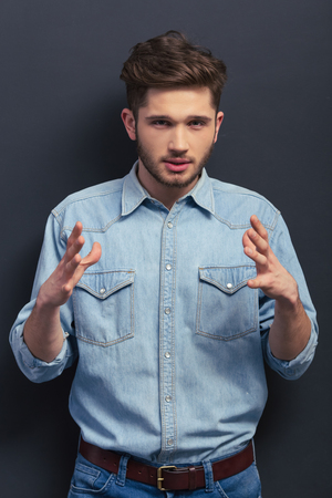 Handsome young student is looking at camera and showing emotions, standing against blackboardの写真素材