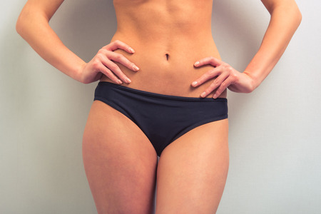 Cropped image of attractive young woman in black underwear standing akimbo against gray background