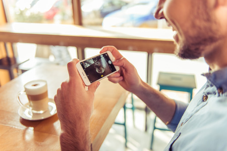 Cropped image of handsome young man making photo of his hot coffee drink using a smartphone and smiling while sitting in the cafeの写真素材