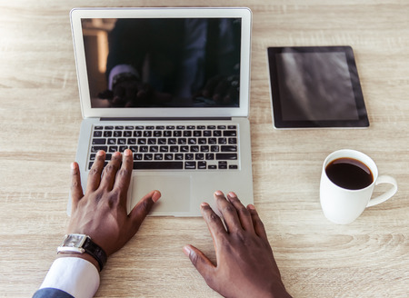 Cropped image of handsome Afro American businessman in classic suit using a laptop while working in officeの写真素材