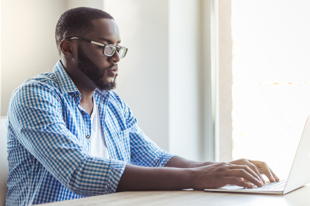 Handsome Afro American businessman in casual clothes and eyeglasses is using a laptop while working at homeの写真素材