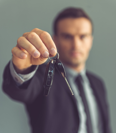 Handsome businessman in classic suit is holding car keys,  on gray background. Hand with keys in focusの写真素材