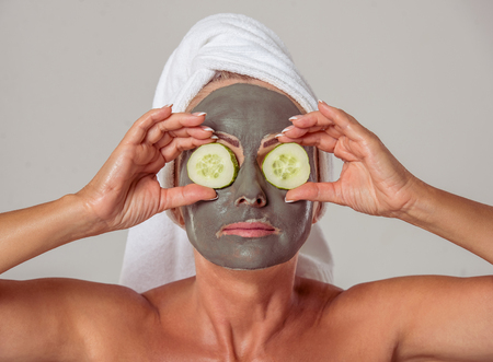 Portrait of beautiful middle aged woman with a towel on her head and a clay mask on her face holding...