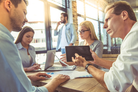 Business people in smart casual wear are discussing affairs and using gadgets while working in the officeの写真素材