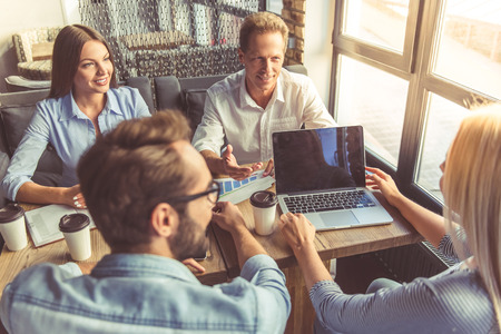Business people in smart casual wear are discussing affairs, using a laptop and smiling while co-working in the cafeの写真素材
