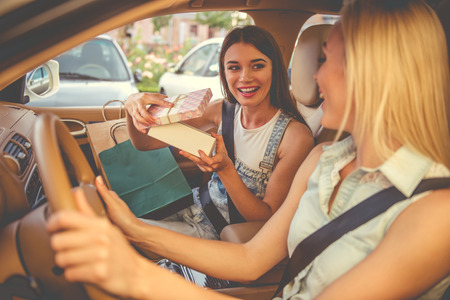 Beautiful stylish girls are examining their purchases and smiling while sitting in the carの写真素材