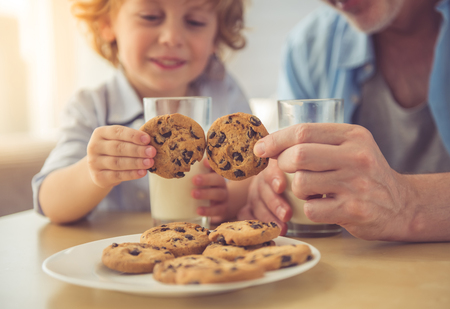 Cropped image of handsome grandpa and grandson drinking milk and eating cookies together at homeの写真素材