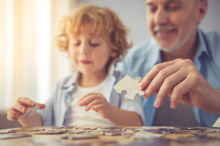 Handsome grandpa and grandson are doing puzzle and smiling while spending time together at homeの写真素材