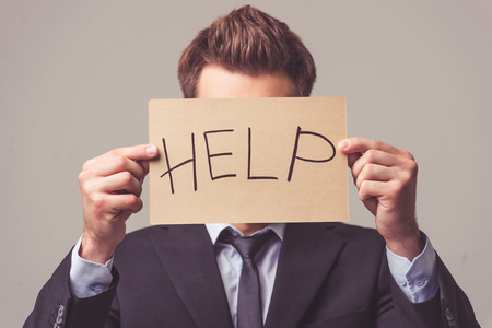 Handsome young businessman in suit is asking for help, on a gray backgroundの写真素材