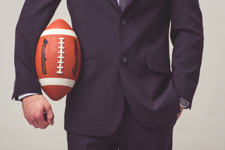 Cropped image of handsome young businessman in suit holding a football ball, on a gray backgroundの写真素材