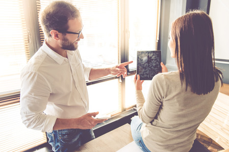 Beautiful business couple is using a digital tablet, talking and smiling while working in officeの写真素材