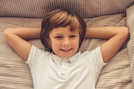Portrait of cute little boy looking at camera and smiling while lying on sofa at homeの写真素材