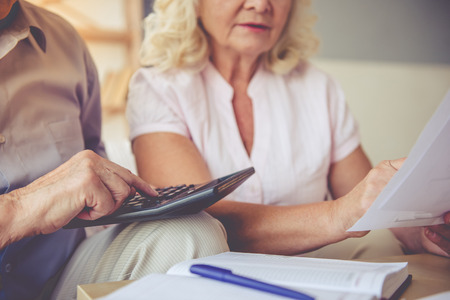 Cropped image of handsome old man and beautiful woman examining documents and using calculator while sitting on couch at homeの写真素材