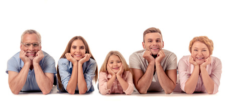 Portrait of cute little girl, her beautiful parents and grandparents leaning on their hands, looking at camera and smiling while lying on the floor, isolated on whiteの写真素材