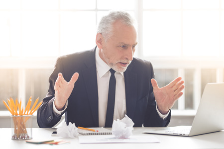 Handsome mature businessman in classic suit is using a laptop while working in his officeの写真素材