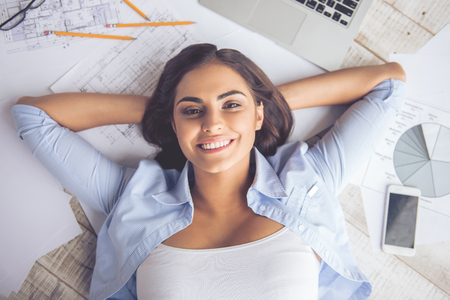 Top view of beautiful business lady looking at camera and smiling while lying on documents on the floor at homeの写真素材