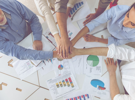 Cropped image of beautiful business people holding hands together while working in office