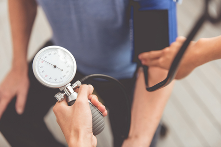 Cropped image of beautiful female doctor in white medical coat testing patient's blood pressure while sitting in officeの写真素材