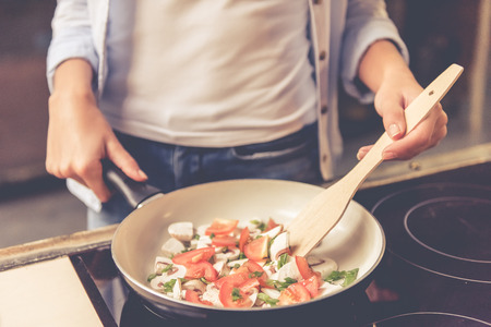 Cropped image of beautiful girl mixing food in frying pan while cooking in kitchen at homeの写真素材