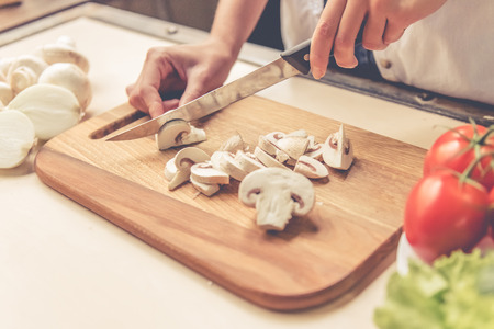 Cropped image of beautiful girl cutting mushrooms while cooking in kitchen at homeの写真素材