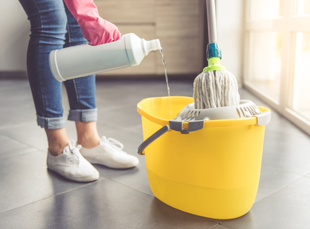 Cropped image of beautiful young woman in protective gloves pouring household chemical into the bucket and using a mop while cleaning floor in the houseの写真素材