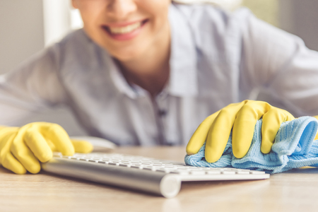 Cropped image of beautiful young woman in protective gloves smiling while wiping keyboard using a...