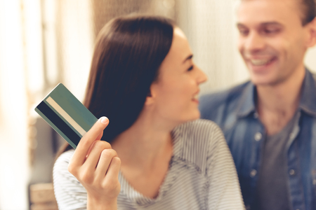 Beautiful young couple is doing shopping online and smiling while resting in cafe. Girl is holding a credit cardの写真素材